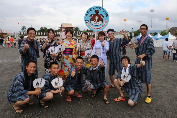 犬山市デカンショ祭りと書かれ、キャラクターが載ったプラカードを持つ、浴衣や甚平を着た男女の写真