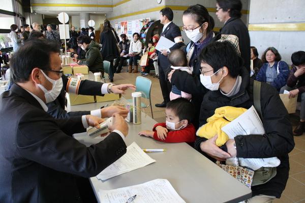 マスクをした家族連れに職員たちがヨウ素剤を渡して説明している写真