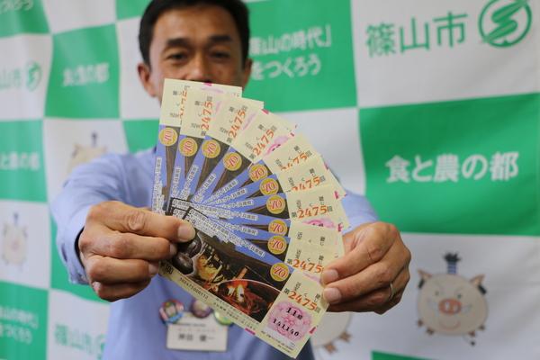 今田町立杭の「最古の登窯」の図柄が採用された複数の宝くじを男性が扇形に広げて手に持っている写真