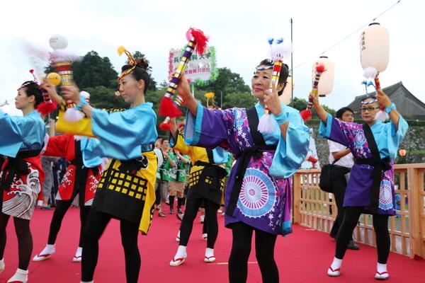 カラフルな法被を着て、装飾された筒を持って踊る女性たちの写真