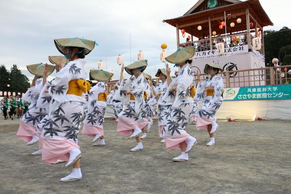 やぐらの前で、編み笠をかぶり、お揃いの浴衣を着ておどる女性の写真