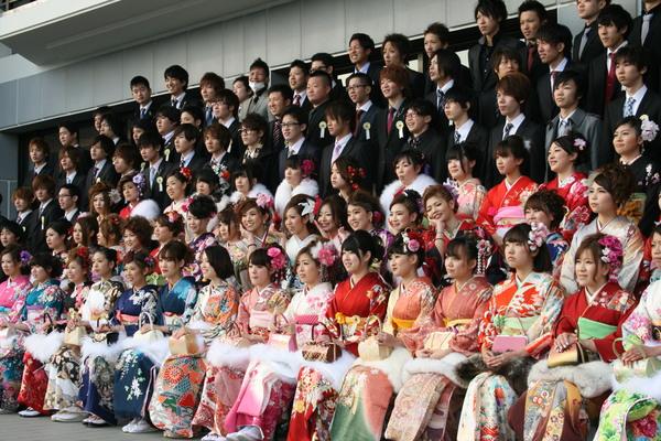 振袖をきている新成人が前の方に座っており、後にはスーツを着た新成人が並んで立っている様子を右下から写している集合写真