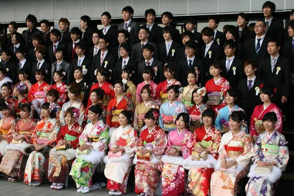 振袖をきている新成人が前の方に座っており、後にはスーツを着た新成人が並んで立っている様子を右上から写している集合写真