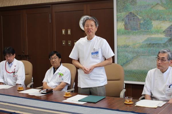 白衣を着た医療従事者3名が椅子に座り、1人が立ち話をしている写真