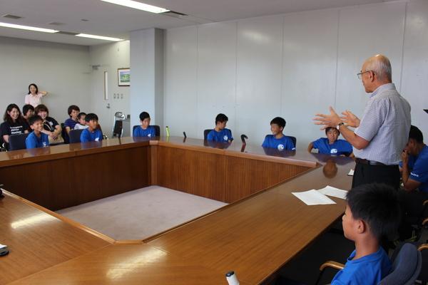 選手と父兄が椅子に座り、市長が立って話をしている写真