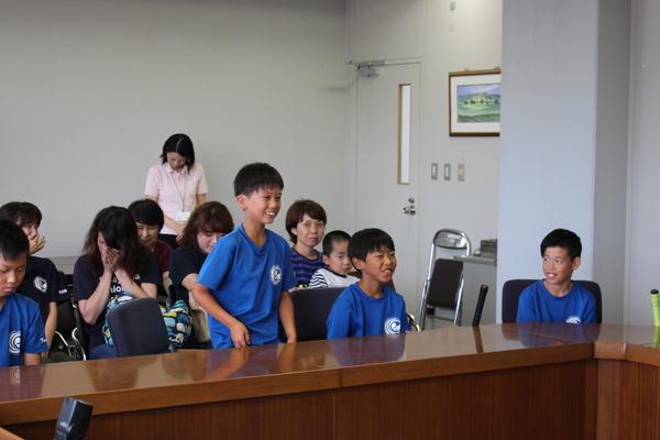 父兄が後ろに座り、その前で男子生徒が立って挨拶をしている写真