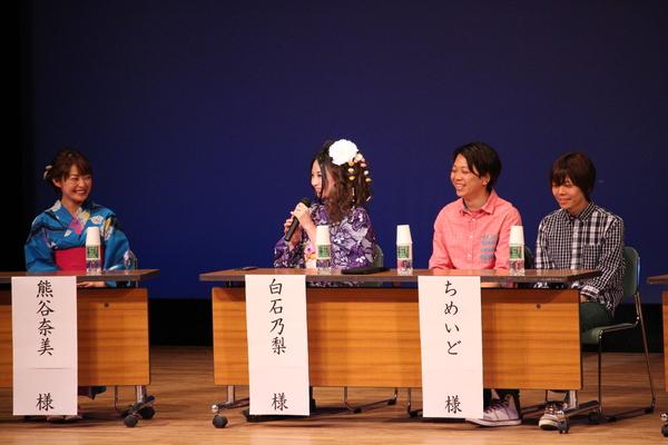 壇上で左からブルーの浴衣姿の熊谷 奈美さんは笑顔で、紫色のちりめん柄の着物姿の白石乃梨さんがマイクを持ち話していてその隣にちめいどささんの二人が座っている写真