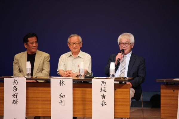 左から南条好輝さん、林 和利さん、西垣 義春さんが壇上にすわり西垣 義春さんがマイクを持ち話をしている写真