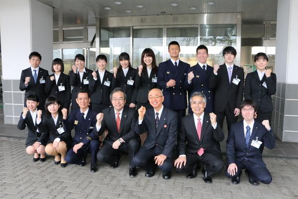 市役所の前で新入社員と市長が右手を上げ記念撮影している写真