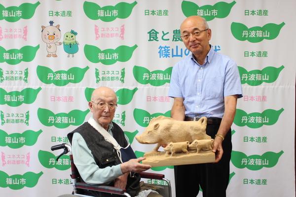 作品創作者の前川さんから市長へ猪の親子の木彫作品を寄贈されている記念写真