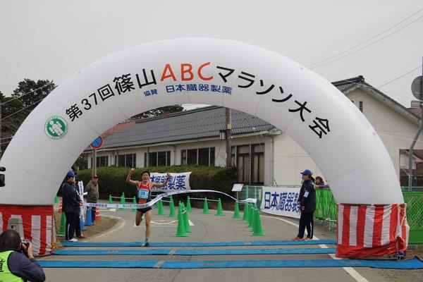 第37回篠山ABCマラソン大会と書かかれたアーチ型のバルーンで出来たゴール地点で1位の選手がゴールテープを切っている写真