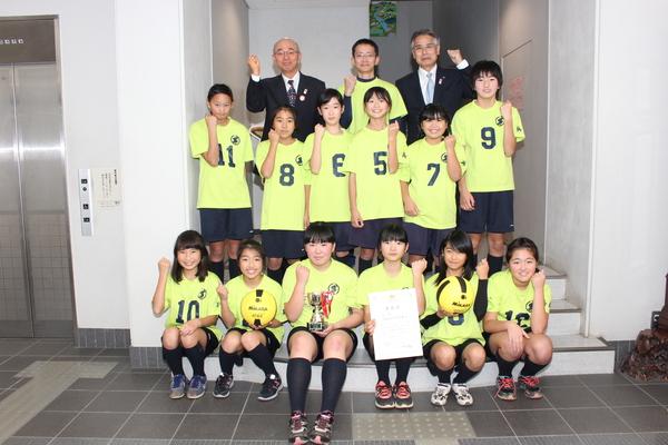 エレベーター横の階段にて、ガッツポーズをする女子生徒たちと市長、関係者の集合写真