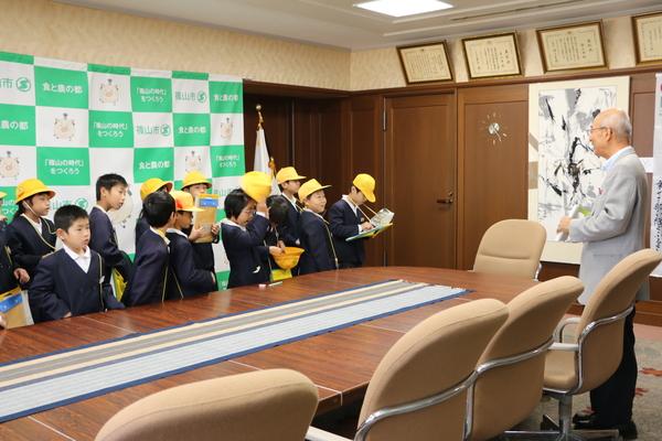 市長室で、制服姿の小学生と市長が向かい合て立っている写真