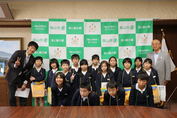 市長と、スーツを着てカメラを首にかけている男性の間に並ぶ小学生の写真