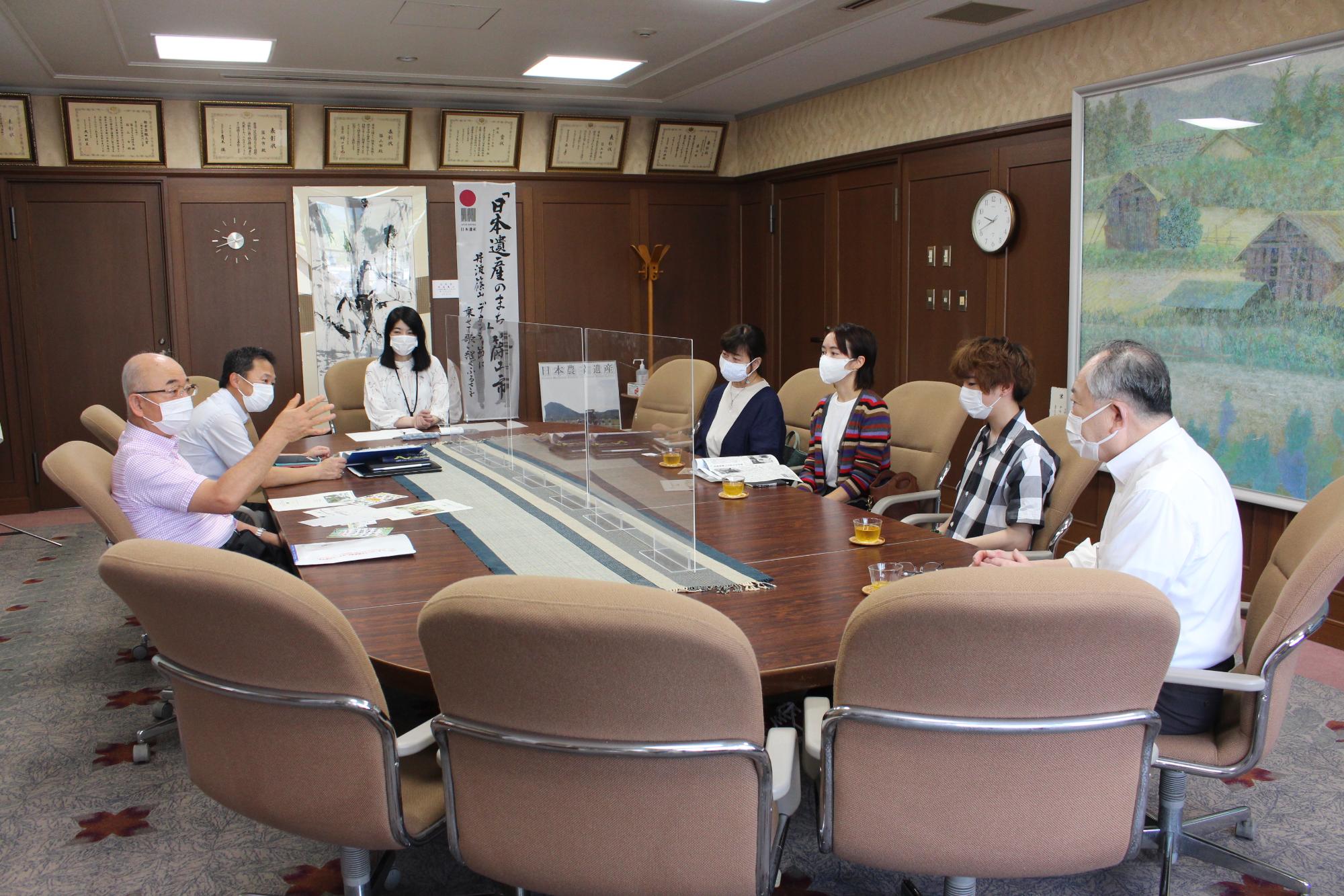 円卓のテーブルで向かい合って7人が話している