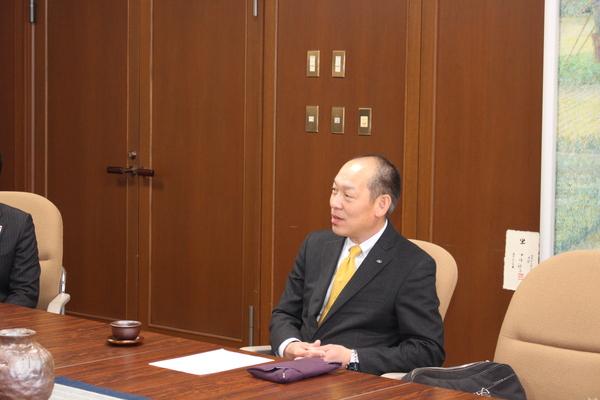 代表取締役社長の降矢 寿民（ふるや としたみ）さんが椅子にすわり机には紫の袱紗が置かれ話をしている写真
