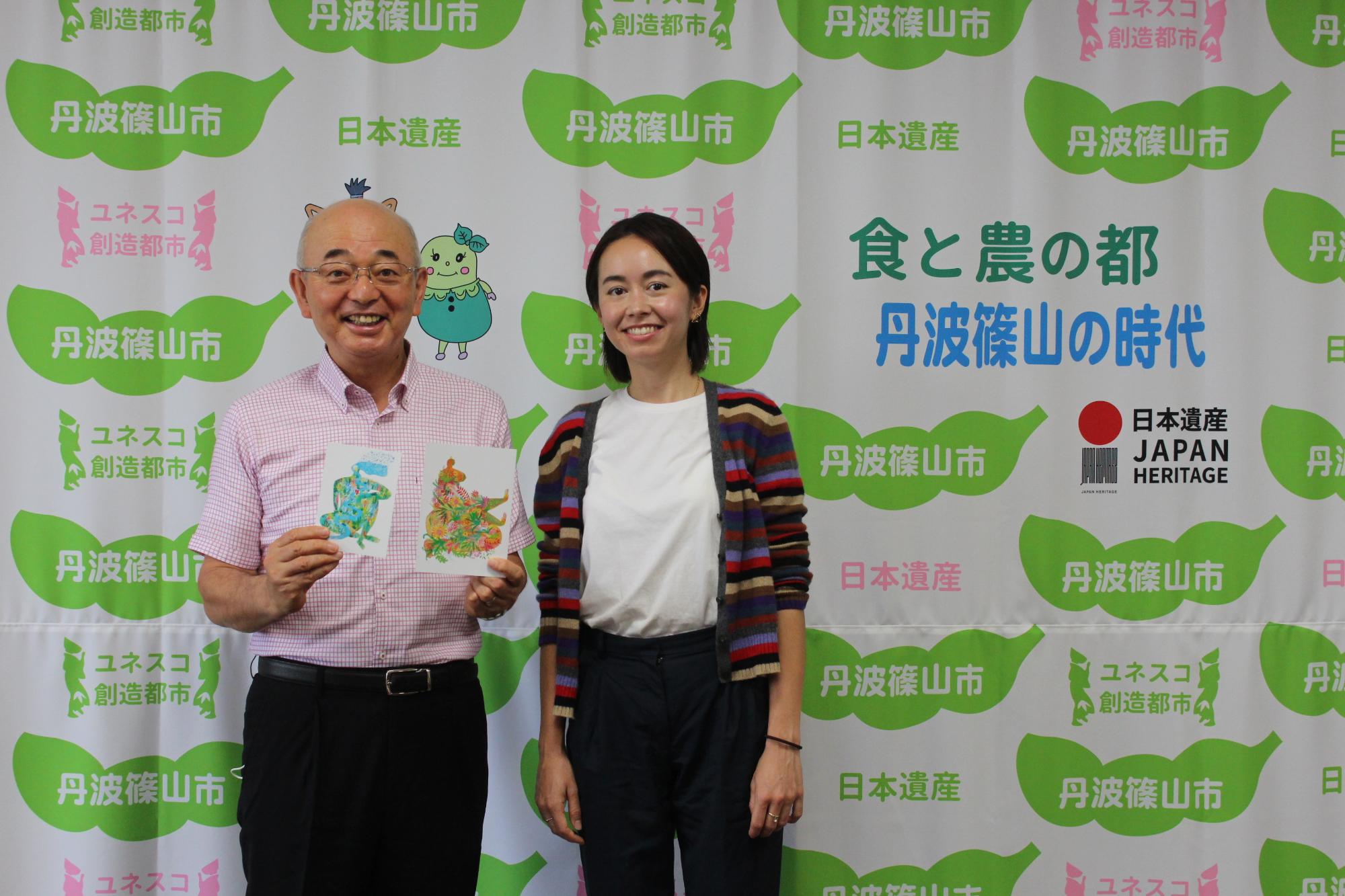 ポストカードを両手に持った市長と女性