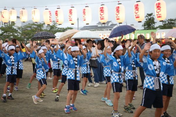 青い祭りの法被を着て、頭に手ぬぐいをまいて躍る子供たちの写真