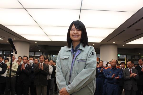 酒井 克美さんが笑顔で前にいて、後ろに職員が並んで拍手している写真