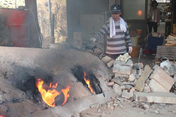 丹波焼やきものを男性が窯で黒い煙をたてながら焼いている写真
