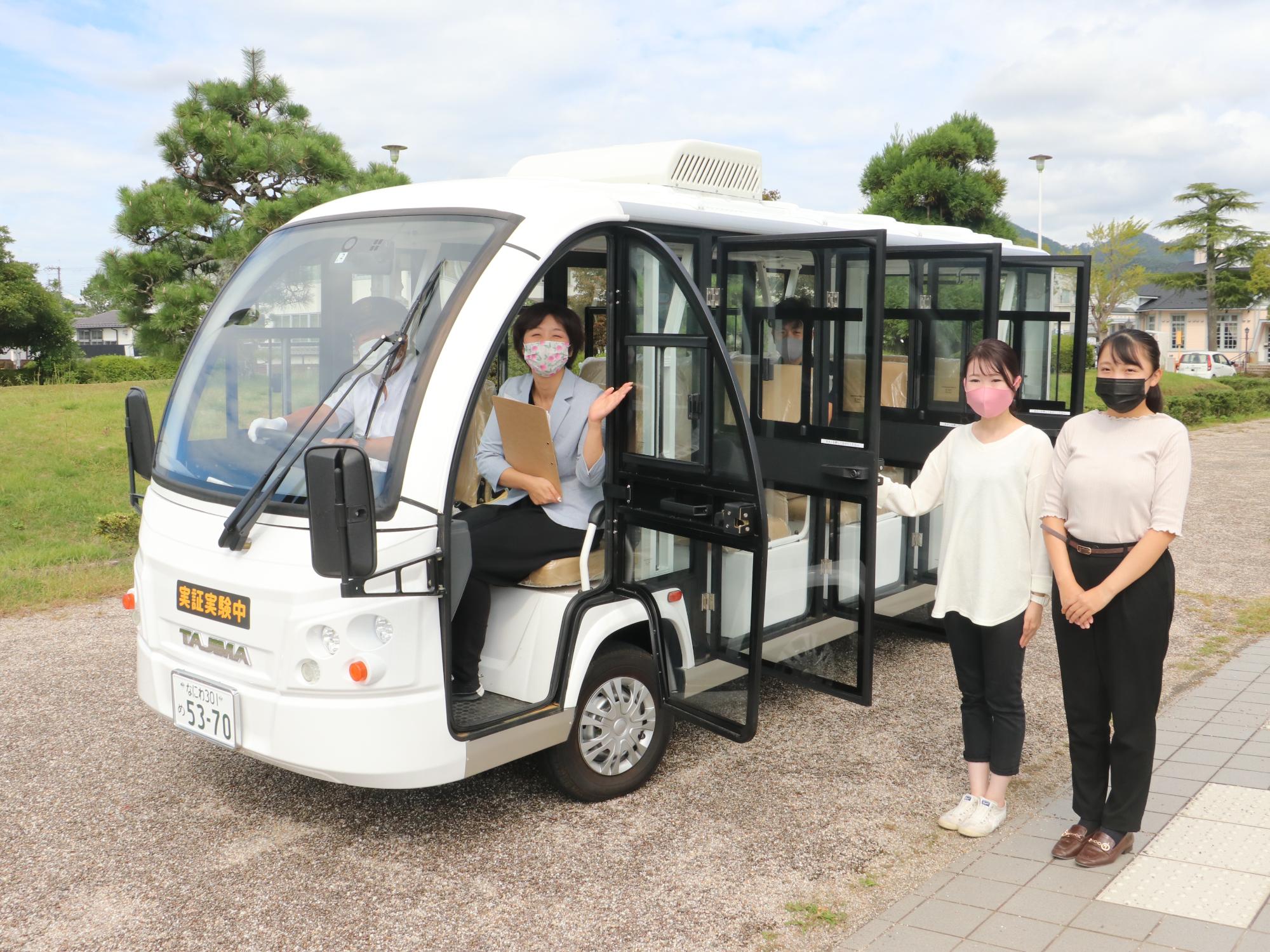 グリーンスローモビリティのドアが開いており、横に女性が二人立っている。車内は運転手と助手席に関係者が乗っている。