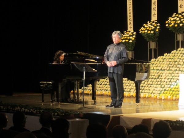 祭壇の前のステージの上でピアノの演奏に合わせて男性が歌を歌っている写真