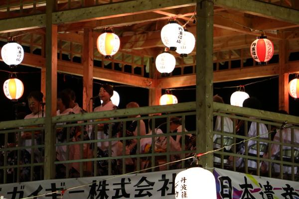 浴衣を着た女性が、やぐらで歌っている写真