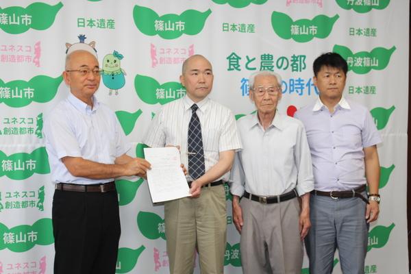 市長と、畑会長が一緒に書類を持ち、顧問の小林さんと役員の酒井さんが横に並んで立っている写真