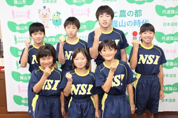 B＆G全国ジュニア水泳競技大会に出場する7名の選手が右腕を曲げて拳を握るポーズを取り笑顔で記念撮影している写真