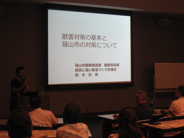大きなモニターに獣害対策の基本と篠山市の対策についてと書かれてあり、その横で講師の男性が話をしている写真