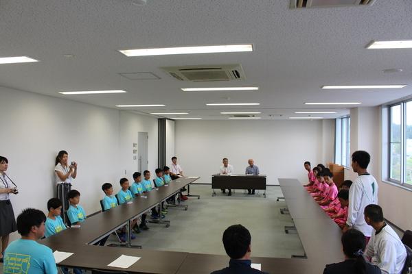 市長を前に向かい合って着席している、水色とピンクのユニフォームを着た男子生徒の写真