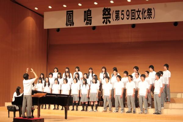 指揮者に合わせピアノが伴奏、生徒達みんなで合唱している写真