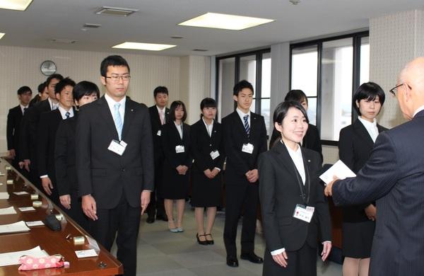 新入写真が並び、市長が代表の新入社員に書類を渡す時の写真