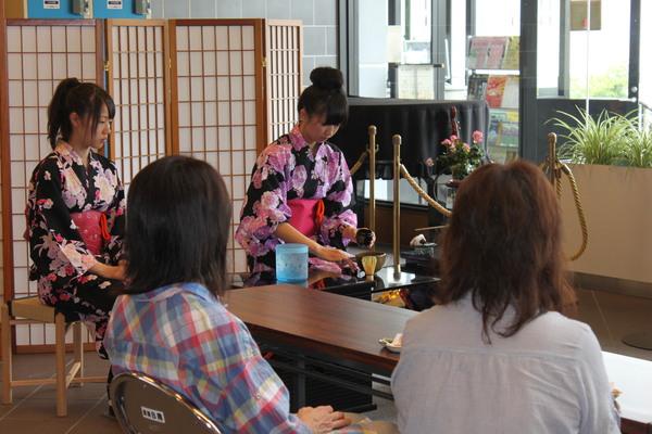 浴衣を着た女の子がお茶をたてて、その姿を父兄が見つめている写真