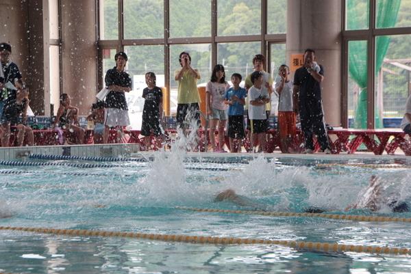 子供達が一生懸命泳いでる所をプールサイドで家族が一生懸命応援している写真