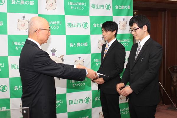 市長から委嘱状を受け取ろうとしている石坂 将一さんとその横に立っている小牧 満也さんの写真
