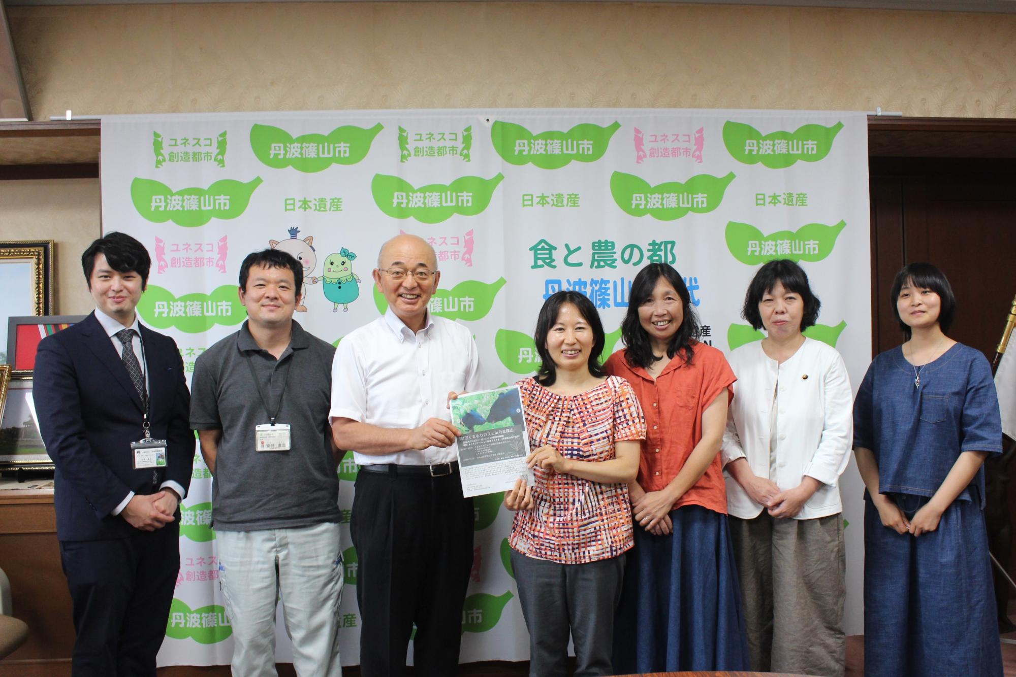 市長と熊森協会の方が一緒にパンフレットを持っている。両隣には市職員や協会の方が並んでいる。