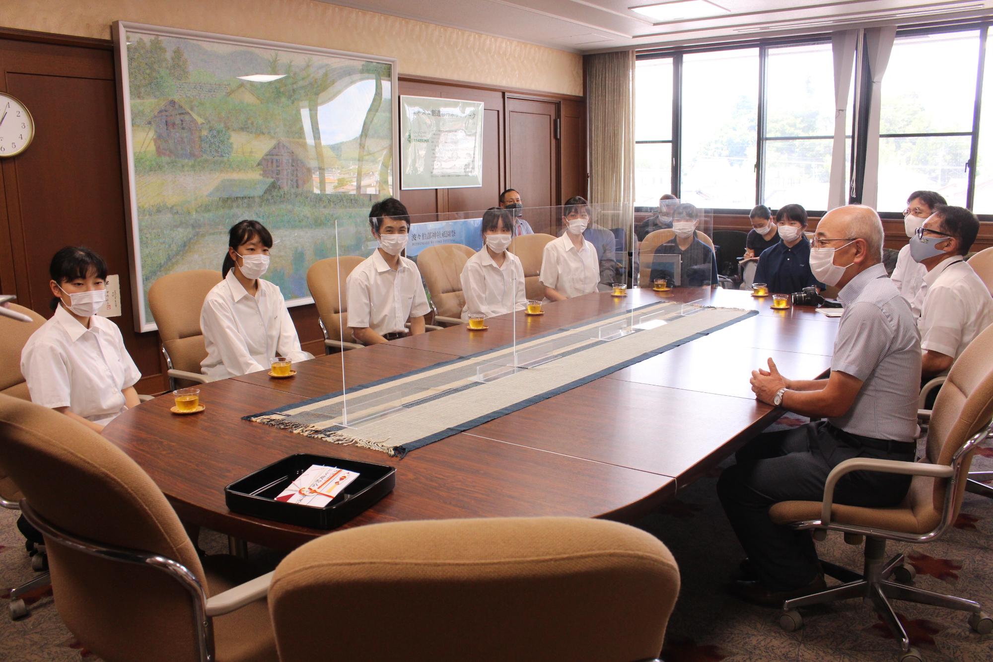 制服を着た高校生たち、市長、教育長が円卓に座って歓談している。