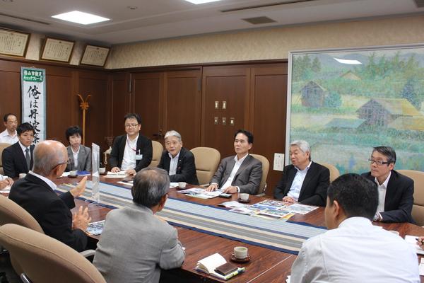 手前には市長が座っていて、その周りに10人ほどのスーツを着た男女がテーブルを囲んで座っている写真