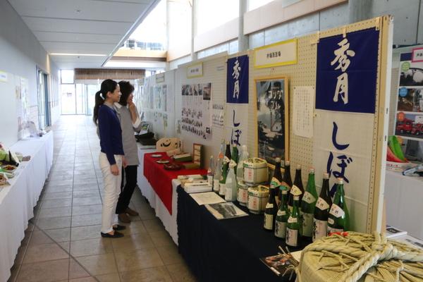 机の上に並べられたお酒や、いろいろな製品、紹介の写真などを見ている女性2名の写真