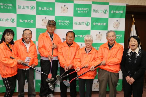 オレンジ色のジャンパーを着た篠山市身体障害者福祉協議会のメンバーが、クラブをそれぞれ持ち、クラブの先を中央に集めて笑顔で写っている様子の写真