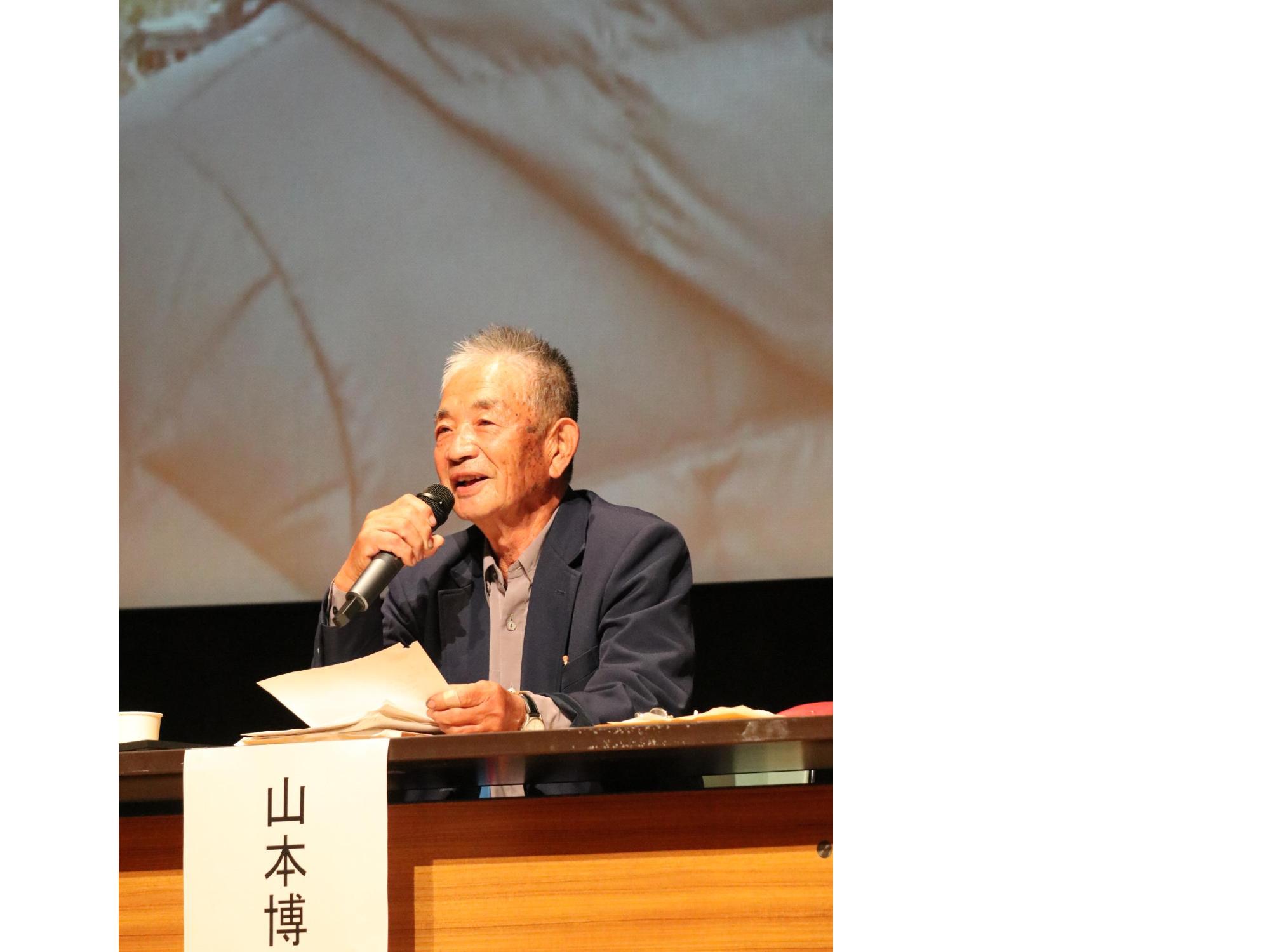 マイクと資料を持った男性が話している