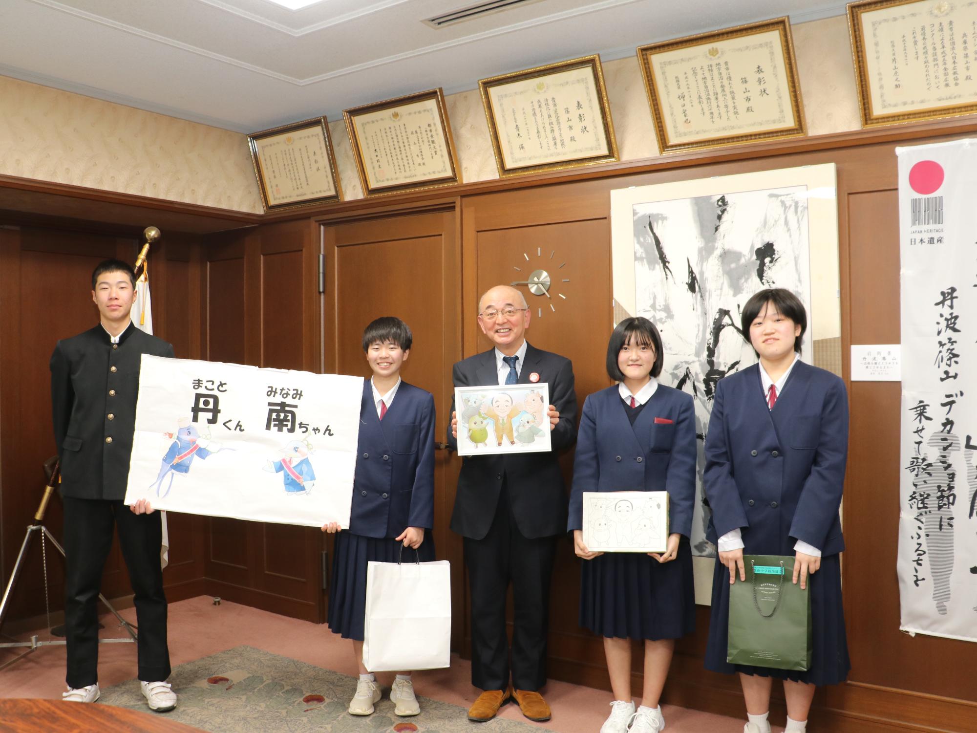 つばめとカワセミをモチーフにしたキャラクターの看板を男の子と女の子が持っていて、その隣に似顔絵を持った市長、女の子人が並んでいる