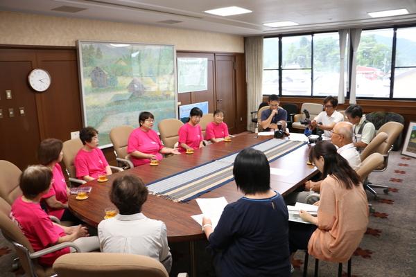 ピンク色のTシャツを着た篠山市いずみ会の女性6名が円卓に座って、中央の女性が市長に話をしている様子の写真