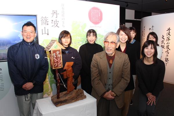 彫刻家の小山 泰二さんと職員の方が作品の周りに並び一緒に笑顔で記念撮影をしている写真