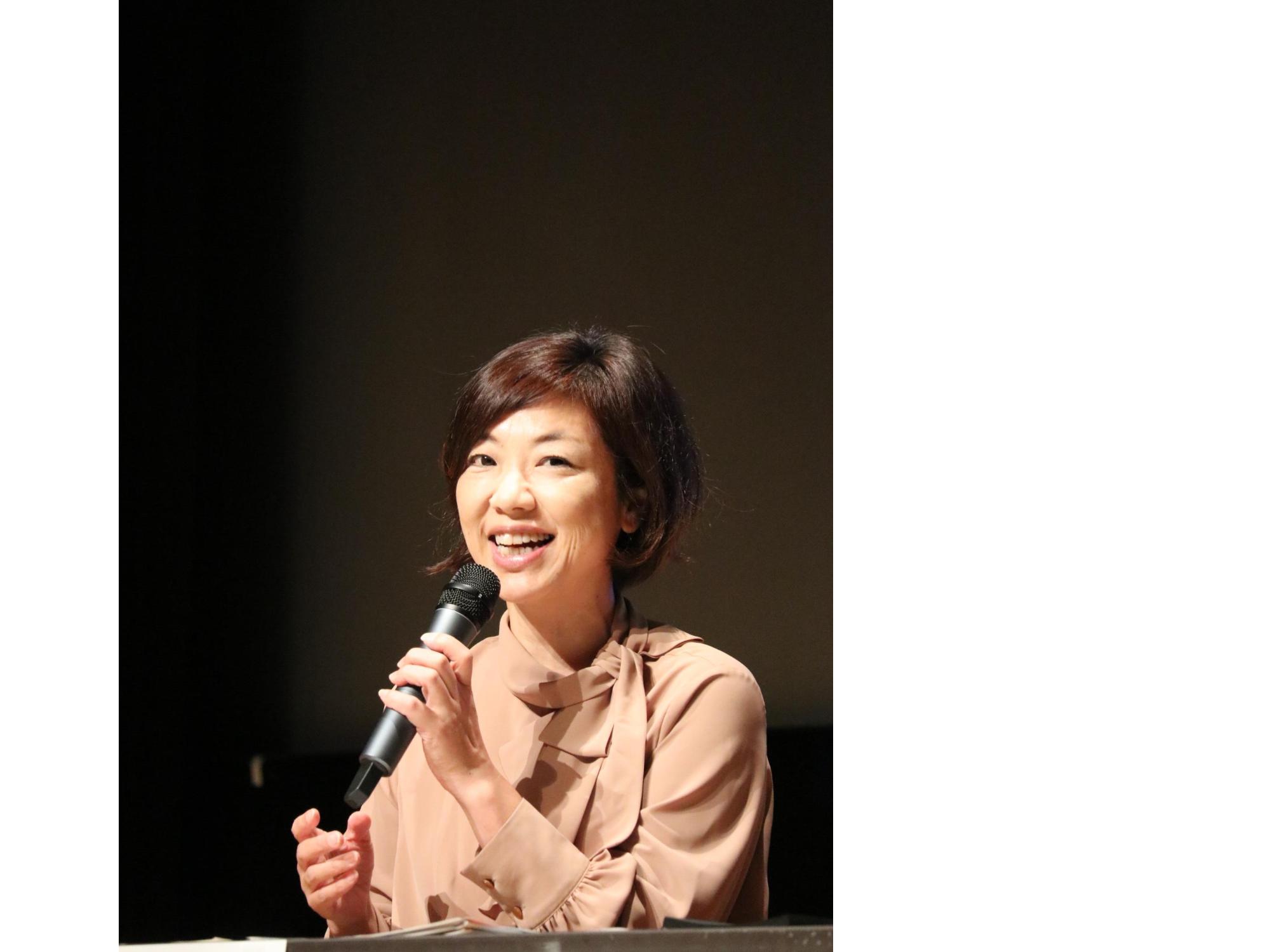 マイクを持った女性が椅子に座って話している