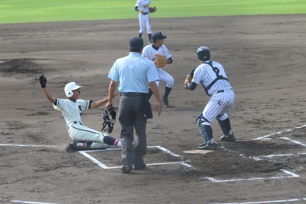 篠山鳳鳴高校軟式野球部の選手が、スライディングをしているなか、相手チームのピッチャーとキャッチャーが右側に向かってボールを投げようとしている写真
