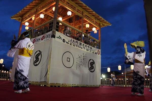 浴衣を着て、編み笠をし、やぐらの周りを踊る女性達の写真