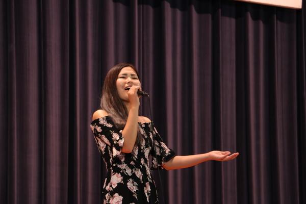 遠山 恵さんがマイクを持ち舞台に手熱唱している写真