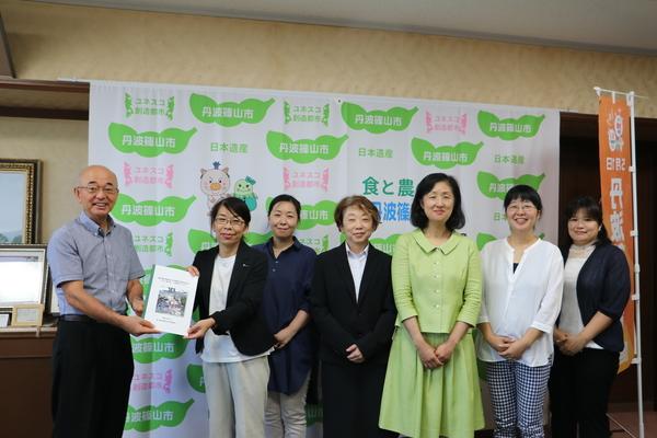 市長と女性委員会の方が提言報告書を持って、女性委員他5名の方も一緒に記念撮影をしている写真